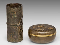 A japanese bronze and gilt relief 'insects among leaves' round bronze box and a tied-scroll-shaped brushpot, meiji period (1868-1912), box ø 12 cm / brushpot h 7 cm