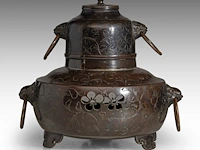 A japanese bronze chagama-shaped koro or incense burner, with floral engraved motifs and shishi heads with rings in their mouths for handles, meiji period (1868-1912), h 19 cm