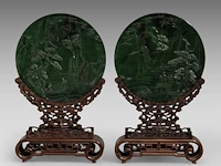 A set of two chinese green jade 'figures in a mountainous landscape' round plaques, fitted as table screens, total h 32,5 cm