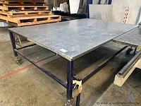 Grote metalen werktafel met een geperforeerd metalen blad. voorzien van wielen.