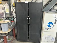 Metalen roldeurkast. de kast is gevuld met diverse materialen, waaronder elektriciteitscomponenten, kabels, tapes en kleine gereedschappen.