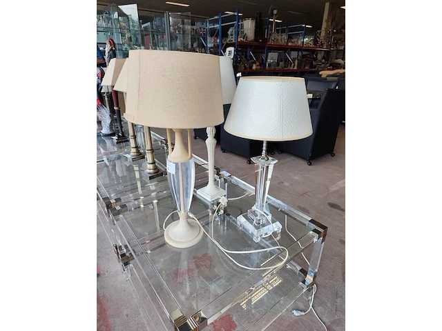 Moderne tafellamp met helder acryl middenstuk en beige stoffen lampenkap riviera maison, moderne tafellamp met kristallen lampenvoet en witte lampenkap met slangenleerstructuur, klassieke tafellamp in oudwit met gedraaide houten voet en beige stoffen kap - afbeelding 1 van  8